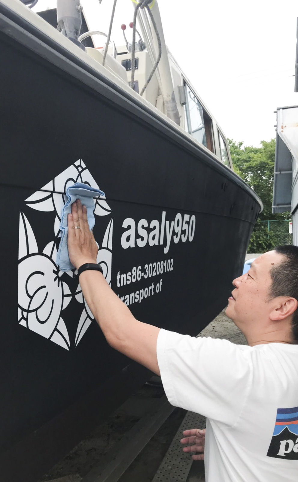 船舶に貼られた白色のカッティングシートを触る男性